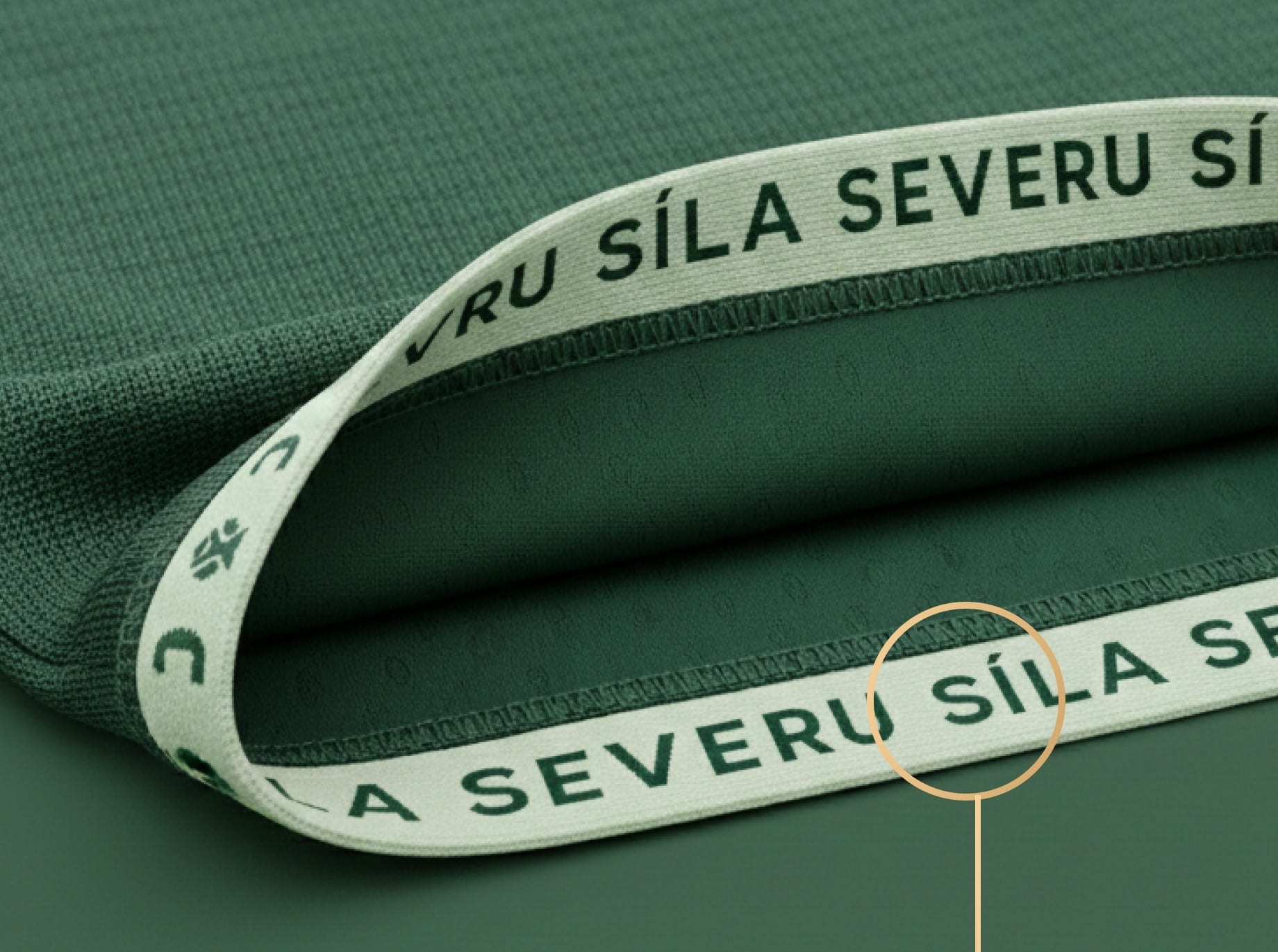 Close-up of a green shirt hem with a pale inner tape reading “SÍLA SEVERU” between tree symbols.