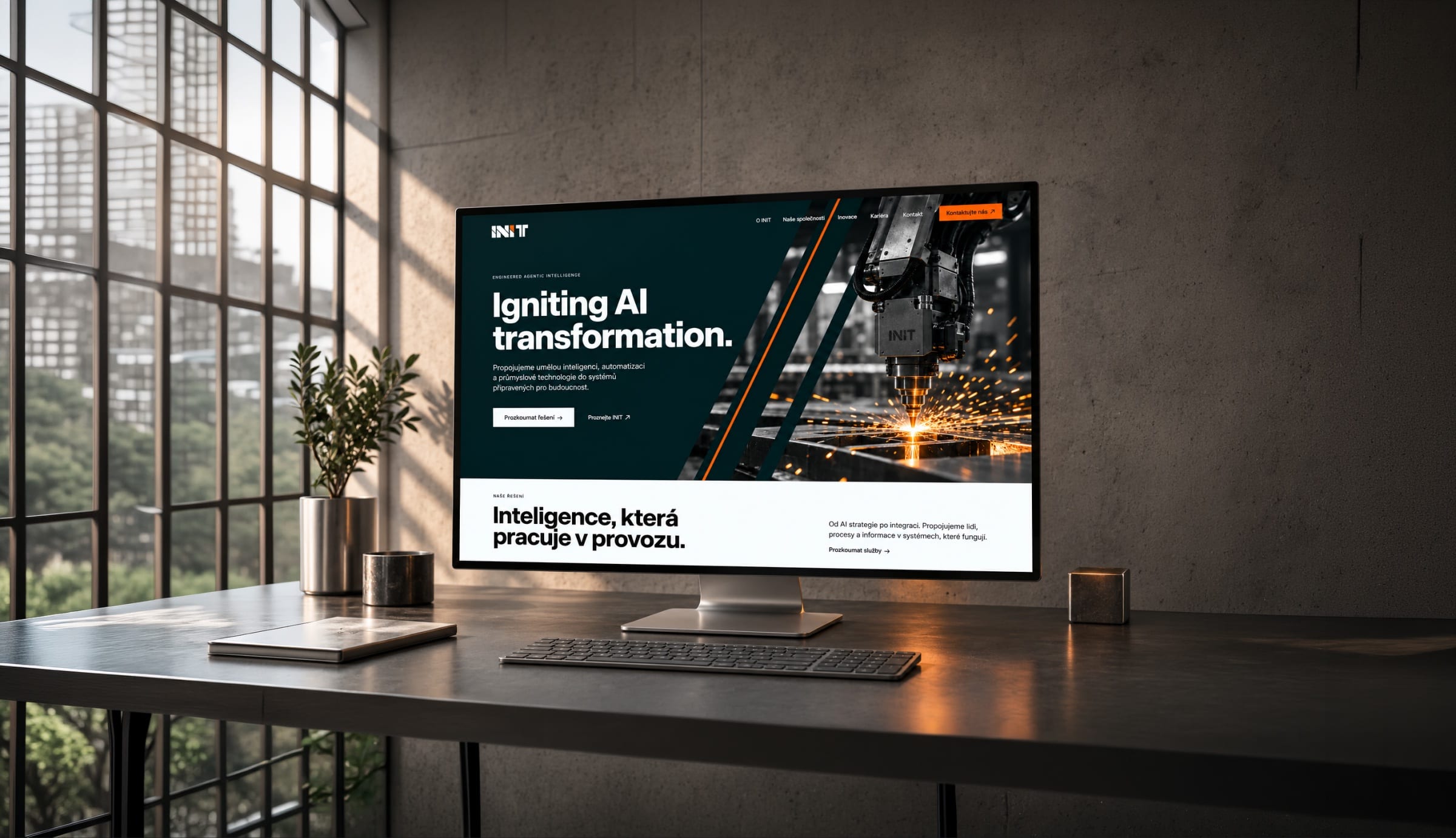 The INIT website on a desktop monitor in a concrete office: Igniting AI transformation over a machine throwing sparks, and below it the Czech line Intelligence that works in operations.