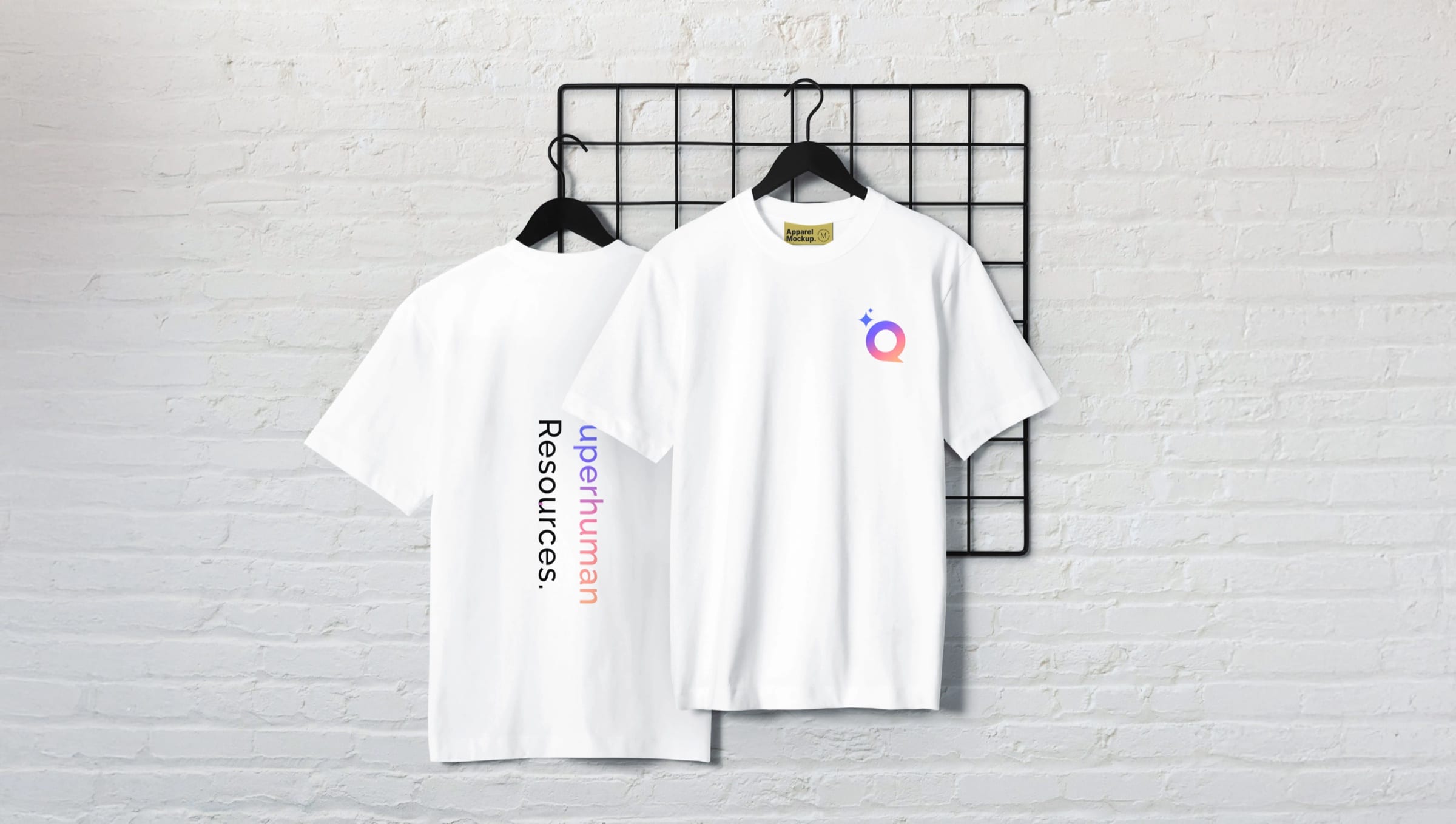 Two white T-shirts on hangers: the Q symbol on the front, “Superhuman Resources.” on the back.