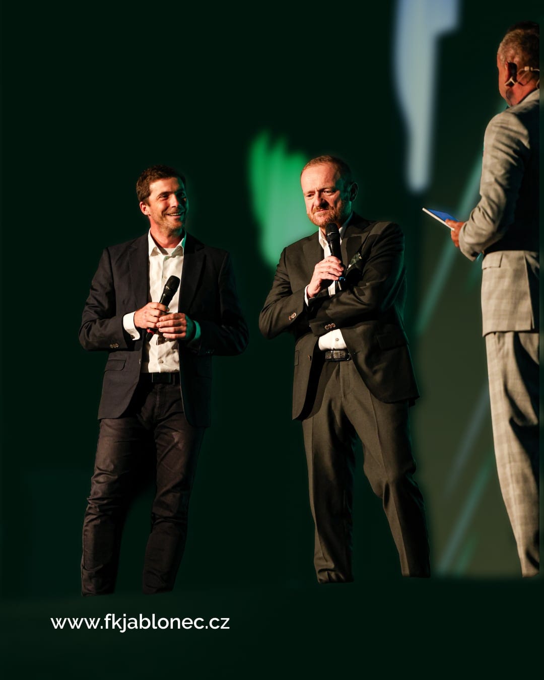Club representatives on stage with microphones at the launch evening, in green light.