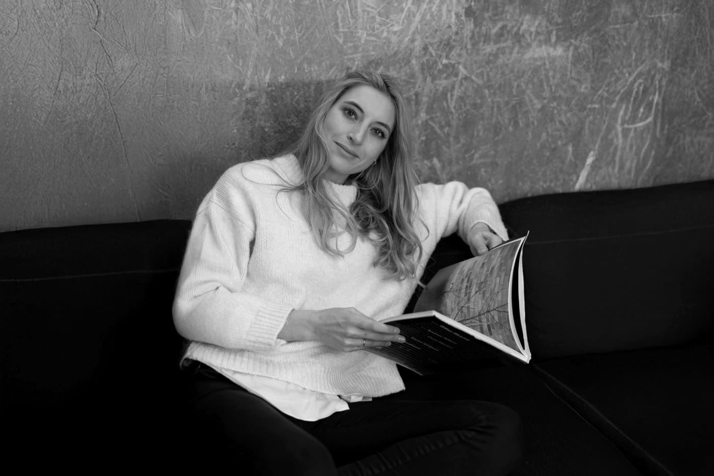 Lucie Krulichová, product and design leader, reading on a dark sofa and smiling at the camera.
